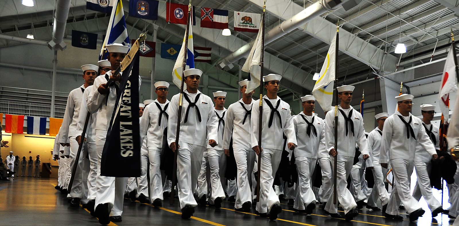 Graduating sailors in dress whites march into the drill hall for Pass in Review at Recruit Training Command Great Lakes