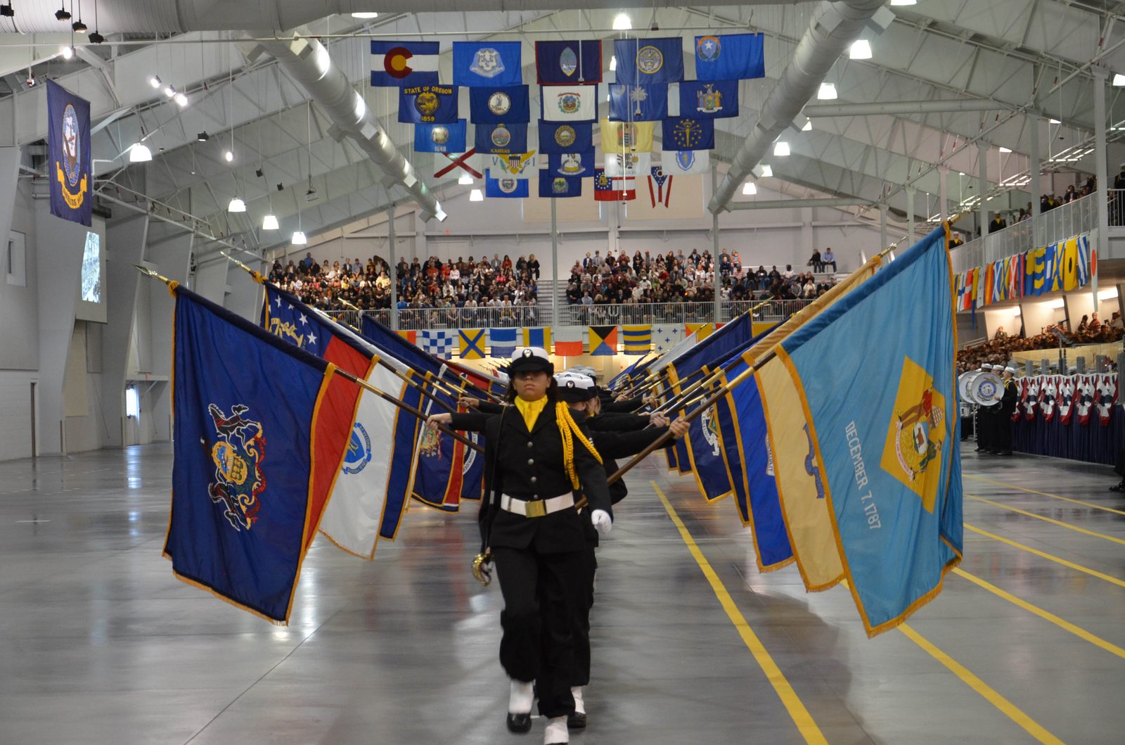 A Navy recruit carries state flags during the Pass in Review ceremony inside the drill hall at Great Lakes