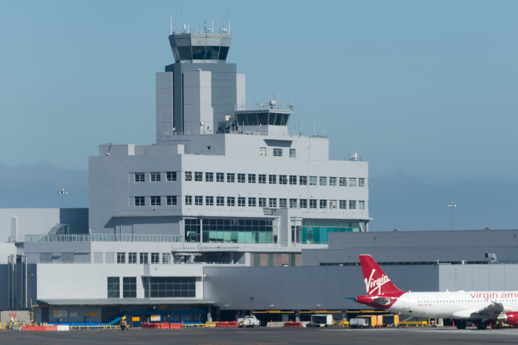 An airport air traffic control tower with an airliner tail in front of it