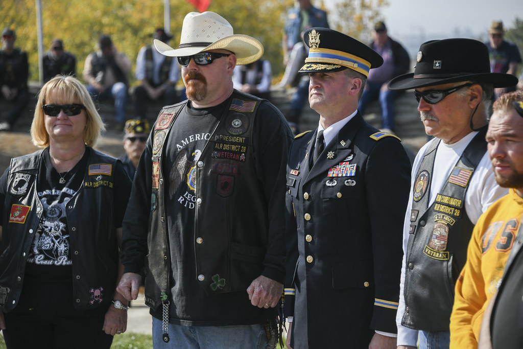 Veterans in service caps and vests greeted by a soldier at a Veterans Day ceremony