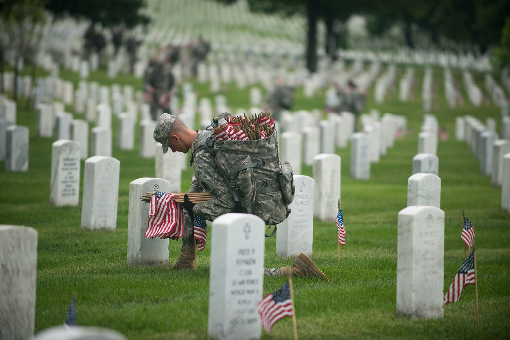 A soldier placing small American flags at headstones in Arlington National Cemetery