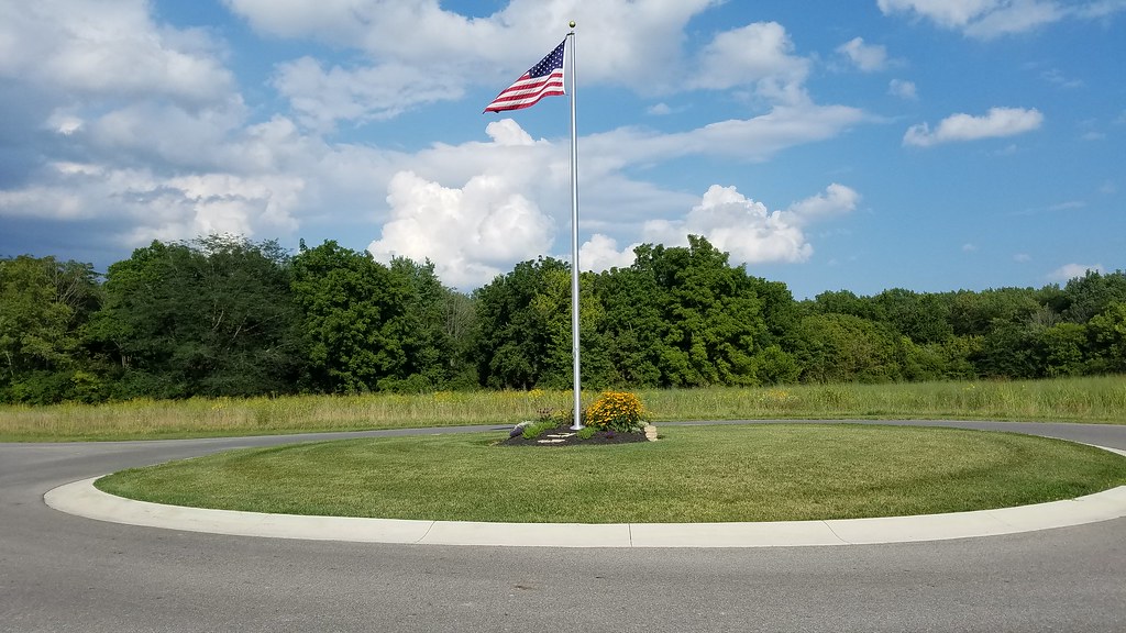 An American flag on a tall flagpole in a park under a blue sky